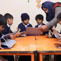 Teacher assisting students with tablets in a tech-enabled classroom.