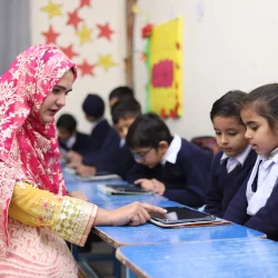 Teacher guiding students on usage of tablet.