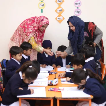 Two teachers helping a group of young students with their studies.